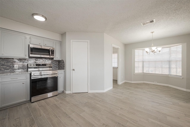 kitchen featuring visible vents, stainless steel appliances, light wood-style floors, a chandelier, and backsplash