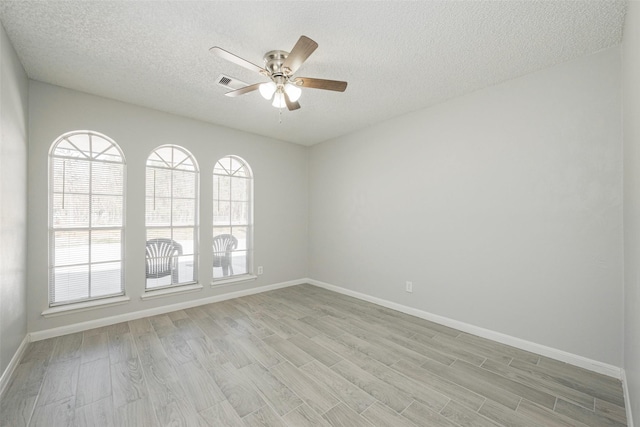 spare room featuring light wood finished floors, visible vents, baseboards, ceiling fan, and a textured ceiling