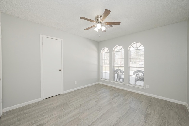 spare room with light wood-style flooring, baseboards, ceiling fan, and a textured ceiling