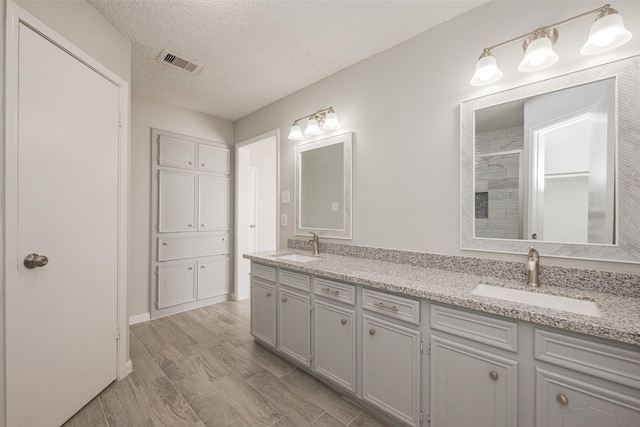 bathroom featuring a textured ceiling, visible vents, a sink, and wood finished floors