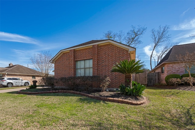 view of home's exterior featuring brick siding, a lawn, and fence