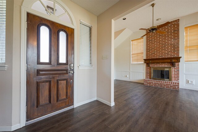 entrance foyer featuring baseboards, a ceiling fan, dark wood-style flooring, a textured ceiling, and a fireplace