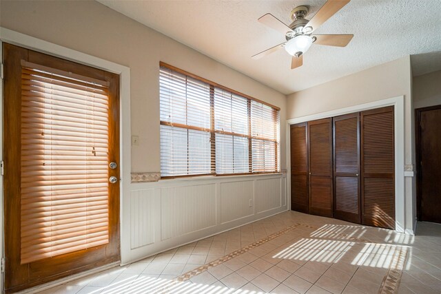 foyer entrance with wainscoting, a ceiling fan, a textured ceiling, and light tile patterned flooring