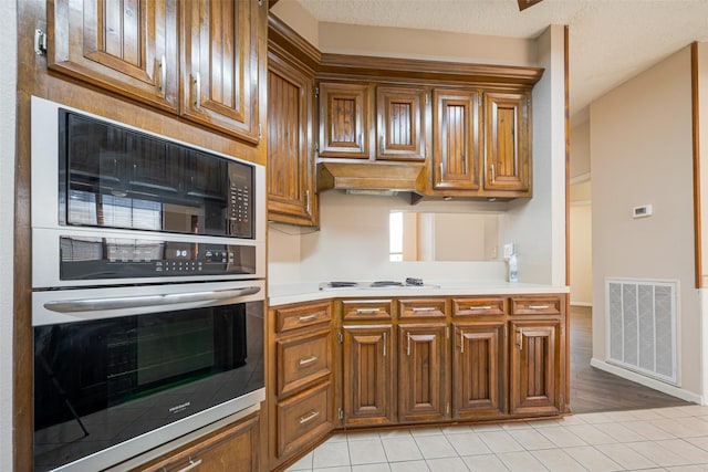 kitchen featuring visible vents, stainless steel oven, brown cabinetry, and light countertops