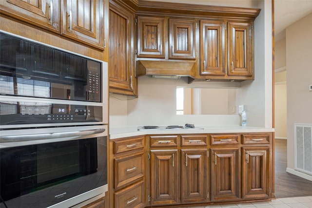 kitchen featuring light countertops, white electric stovetop, visible vents, and brown cabinets