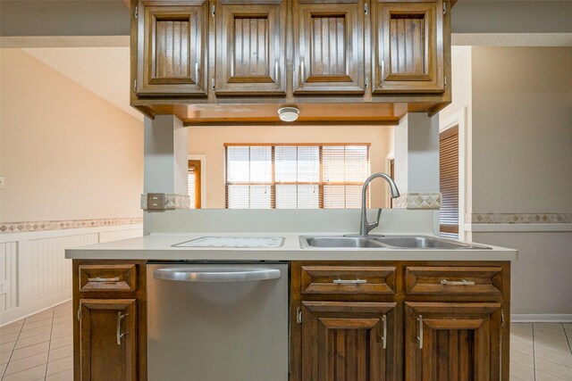 kitchen with a sink, light tile patterned flooring, dishwasher, and wainscoting