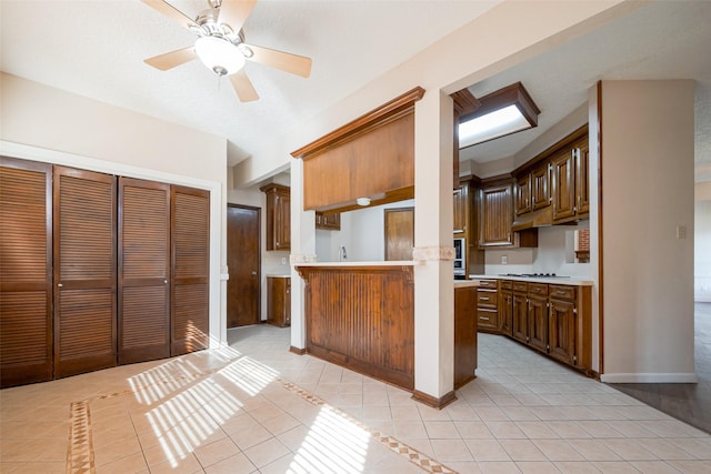 kitchen with a ceiling fan, a peninsula, light countertops, stainless steel gas cooktop, and light tile patterned flooring