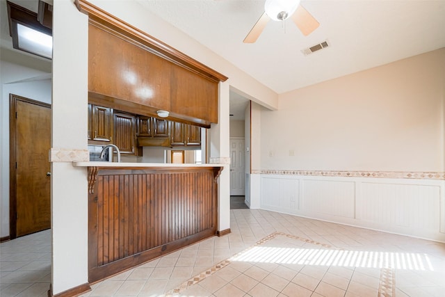 kitchen with light tile patterned floors, visible vents, wainscoting, light countertops, and a sink