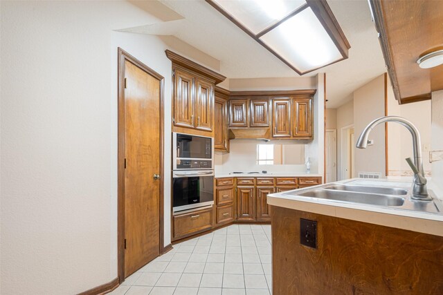 kitchen featuring light tile patterned floors, brown cabinets, oven, black microwave, and a sink