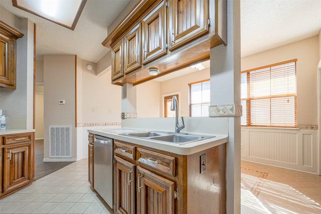 kitchen featuring visible vents, brown cabinetry, light tile patterned flooring, a sink, and dishwasher