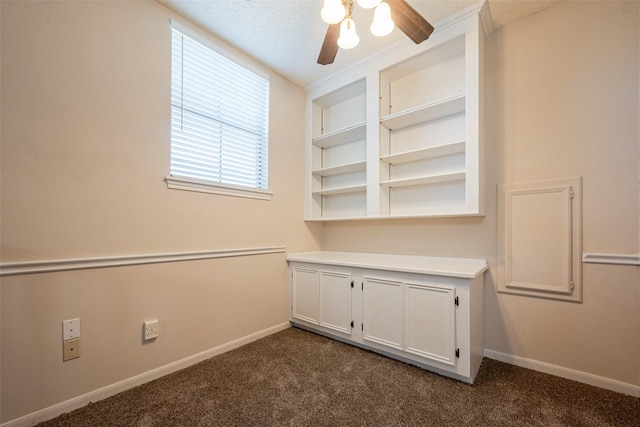 empty room featuring baseboards, a textured ceiling, dark carpet, and a ceiling fan