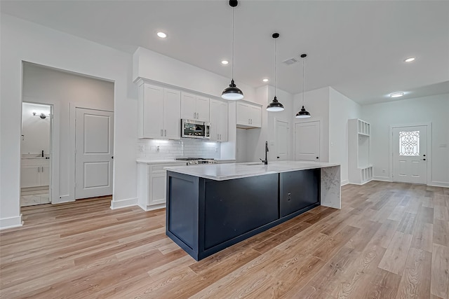 kitchen with white cabinetry, stainless steel microwave, light countertops, and decorative backsplash