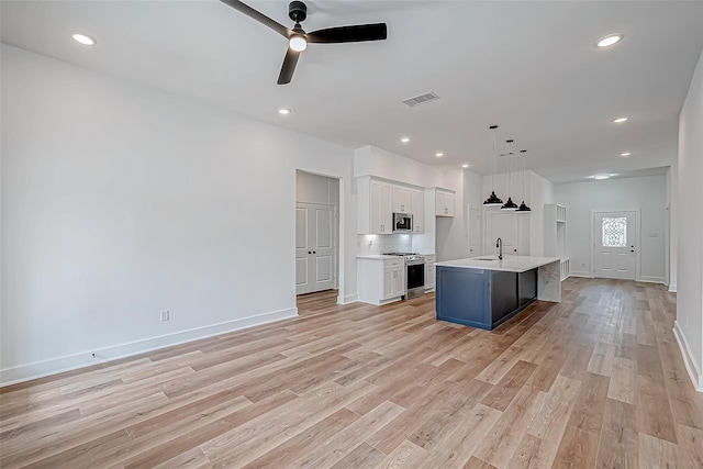 kitchen with white cabinets, appliances with stainless steel finishes, light countertops, light wood-type flooring, and a sink