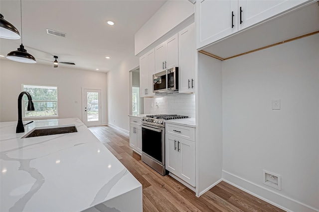 kitchen featuring light stone counters, visible vents, decorative backsplash, appliances with stainless steel finishes, and a sink