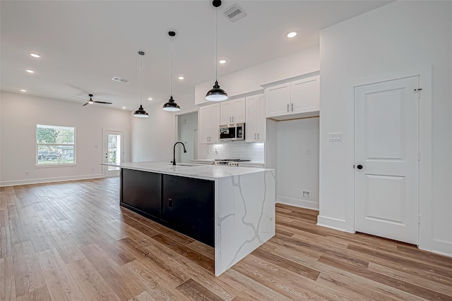 kitchen featuring light wood finished floors, tasteful backsplash, stainless steel microwave, visible vents, and a sink