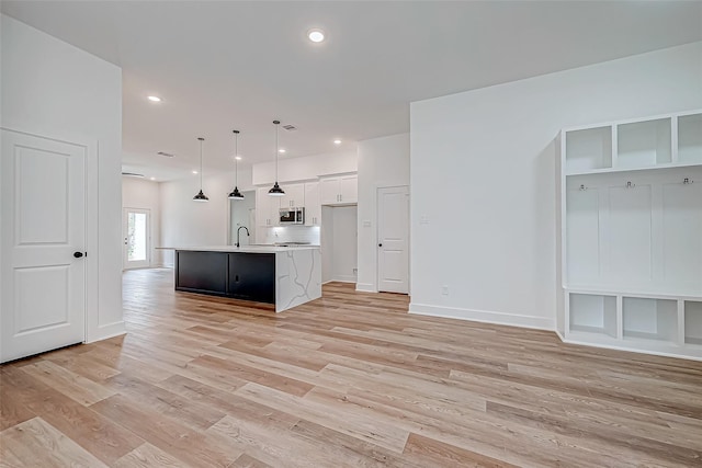 kitchen featuring light countertops, stainless steel microwave, white cabinetry, a kitchen island with sink, and light wood-type flooring