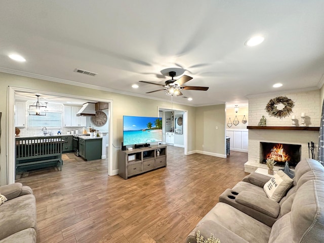 living area with a brick fireplace, wood finished floors, visible vents, and crown molding