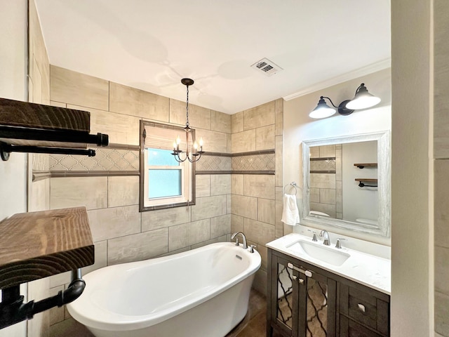 bathroom with visible vents, a freestanding bath, vanity, a chandelier, and tile walls