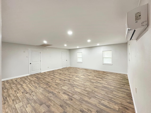 below grade area with recessed lighting, wood finished floors, visible vents, baseboards, and a wall mounted air conditioner