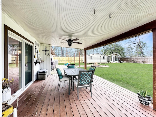 wooden terrace featuring an outbuilding, outdoor dining area, a yard, ceiling fan, and a fenced backyard