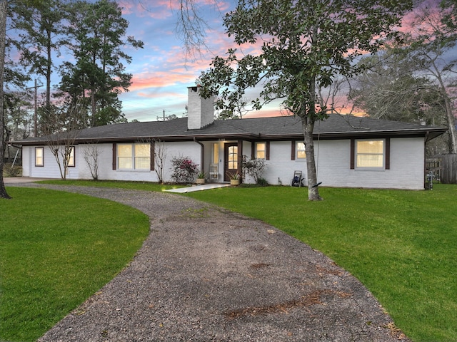 ranch-style home with gravel driveway, a chimney, and a front yard