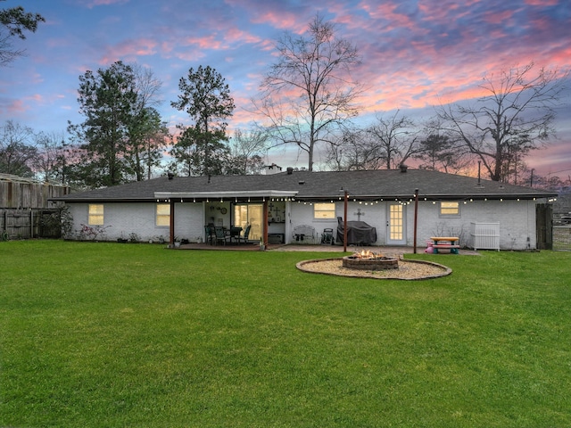 back of house at dusk with a fire pit, a yard, a patio, and fence