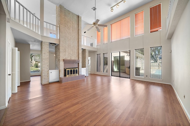 unfurnished living room featuring ceiling fan, a fireplace, wood finished floors, baseboards, and rail lighting