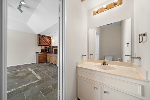 bathroom featuring toilet, vanity, baseboards, vaulted ceiling, and stone finish flooring