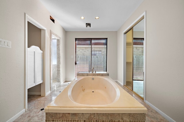 bathroom featuring baseboards, a textured wall, and a tub with jets