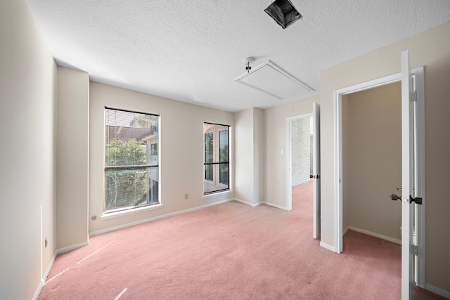 spare room with attic access, light colored carpet, a textured ceiling, and baseboards