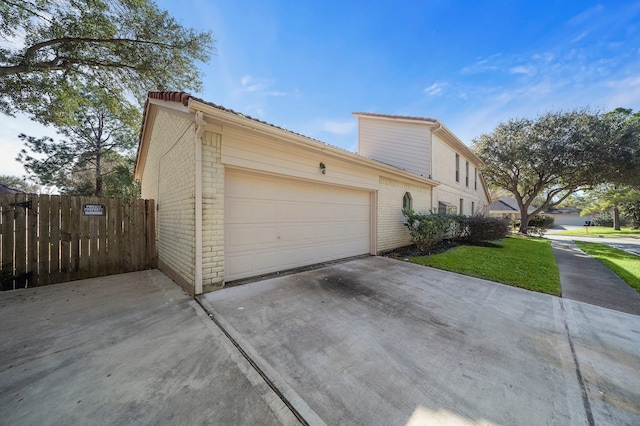 view of side of property with an attached garage, brick siding, fence, a yard, and concrete driveway