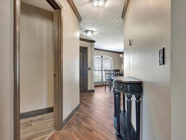 corridor with a textured ceiling, a textured wall, wood finished floors, baseboards, and crown molding