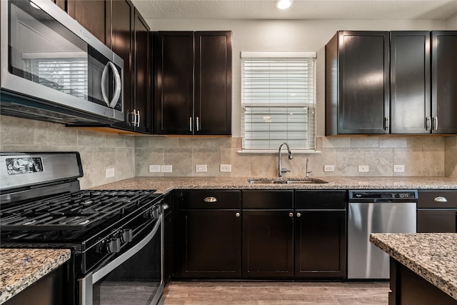 kitchen featuring light stone counters, appliances with stainless steel finishes, decorative backsplash, and a sink