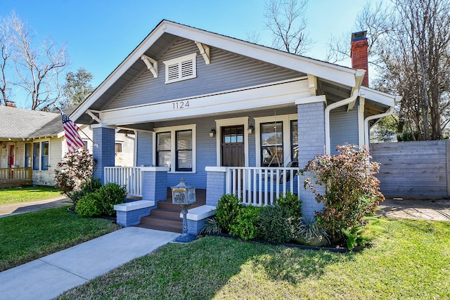 bungalow-style home featuring covered porch, a front lawn, a chimney, and fence