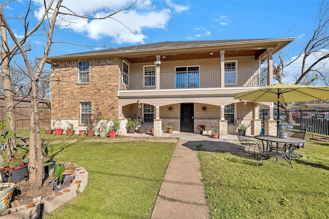 view of front facade with brick siding, a balcony, a front lawn, and fence