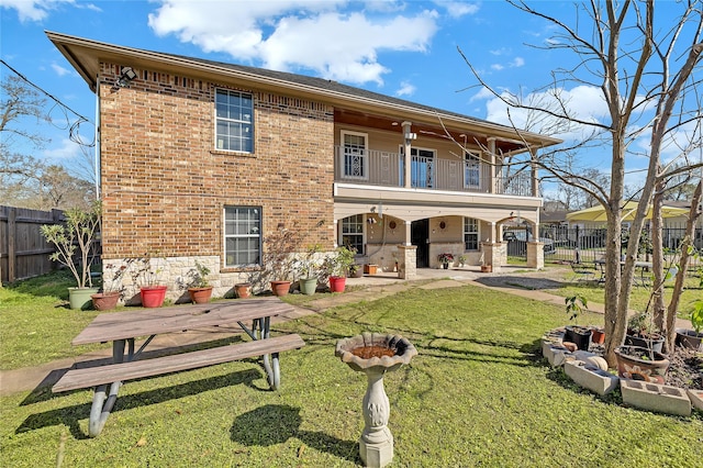 back of property with a balcony, a yard, fence, and brick siding