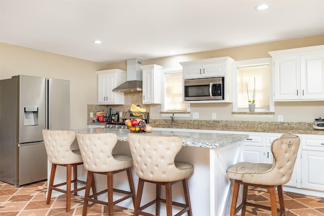 kitchen with tasteful backsplash, a center island, white cabinetry, appliances with stainless steel finishes, and wall chimney exhaust hood