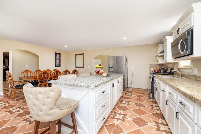 kitchen with a sink, a kitchen breakfast bar, a kitchen island, white cabinetry, and stainless steel appliances