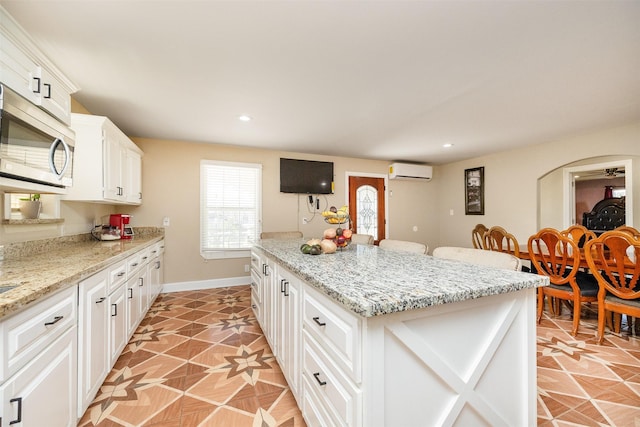 kitchen with a wall mounted air conditioner, stainless steel microwave, a center island, white cabinetry, and baseboards