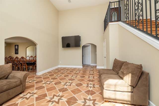 living room with arched walkways, stairway, baseboards, and a towering ceiling