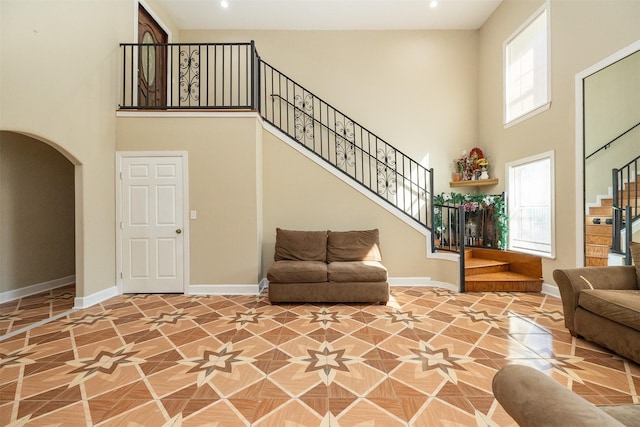 living area with stairs, a high ceiling, baseboards, and arched walkways