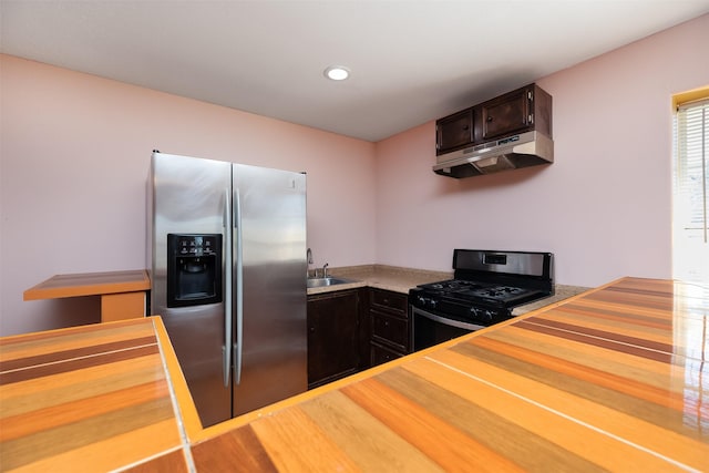 kitchen with under cabinet range hood, a sink, wood finished floors, appliances with stainless steel finishes, and dark brown cabinets