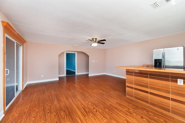 unfurnished living room featuring arched walkways, visible vents, baseboards, and dark wood-style flooring