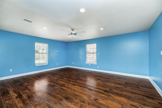 unfurnished room featuring a wealth of natural light, visible vents, baseboards, and dark wood-style floors