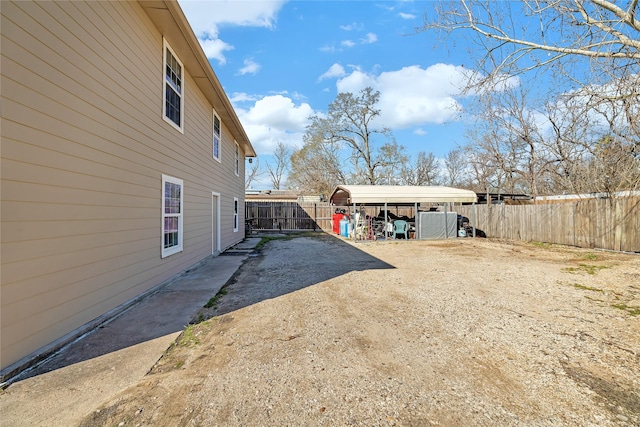 view of yard with dirt driveway, a detached carport, and fence