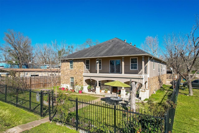 back of property with brick siding, a fenced front yard, a yard, a balcony, and a patio