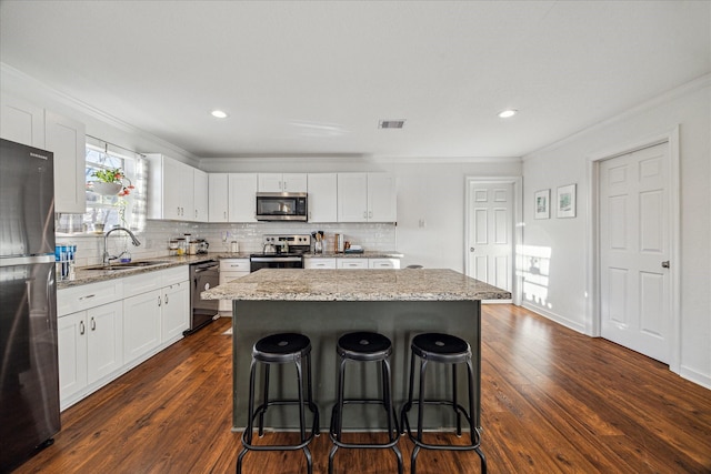 kitchen featuring white cabinets, a kitchen island, appliances with stainless steel finishes, a breakfast bar, and a sink