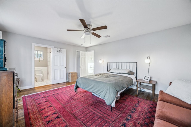 bedroom featuring visible vents, ensuite bath, baseboards, and wood finished floors