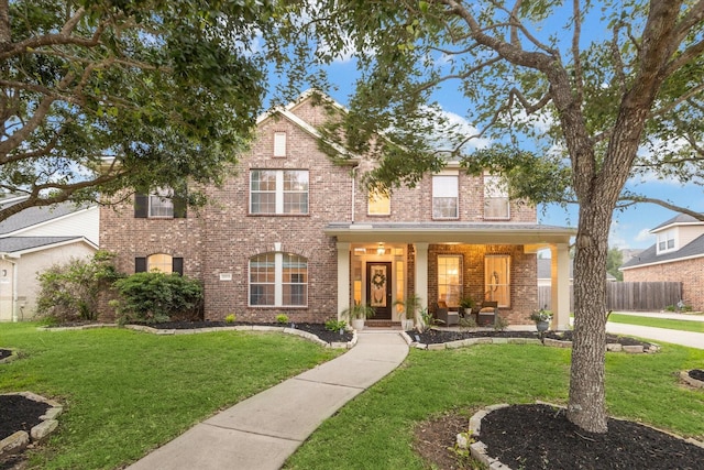 view of front of property with a front lawn, a porch, fence, and brick siding