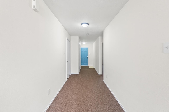 hall featuring dark colored carpet and baseboards